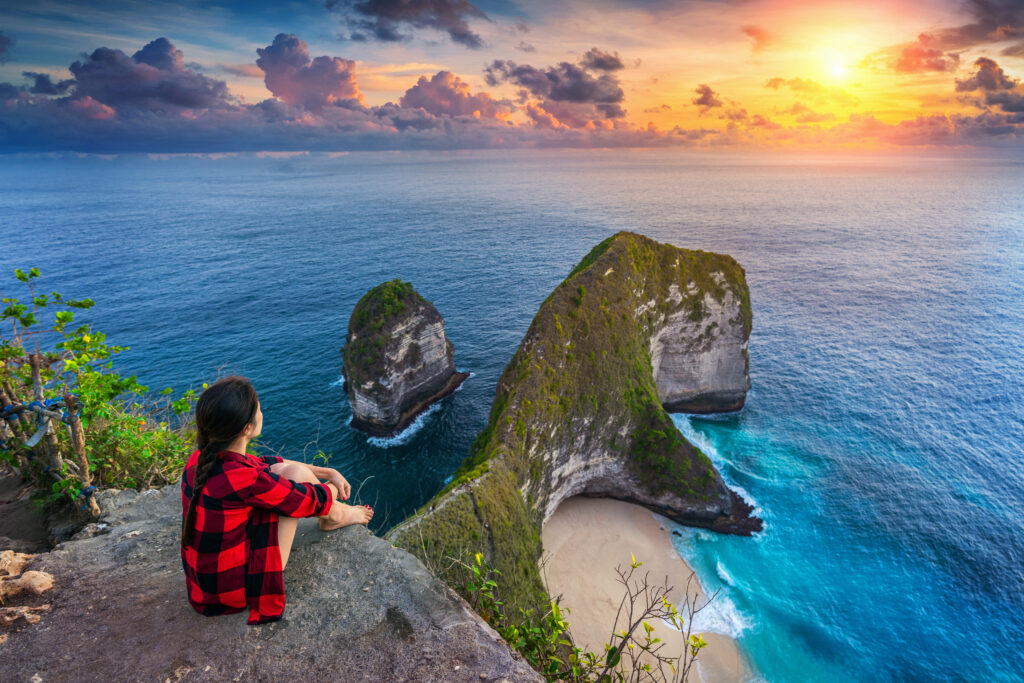 Woman sitting on cliff and looking at sunset at Kelingking Beach
